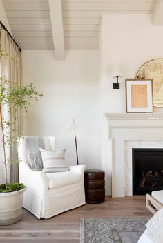 a living room with white furniture and a fire place in the corner, along with a potted plant