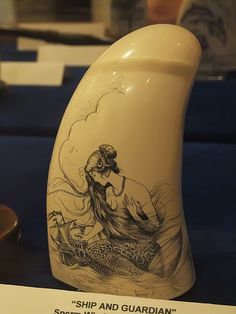 a white vase with an image of a mermaid sitting on it's side and the words ship and guardian written below