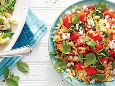 two plates of pasta with vegetables and feta cheese on the side, next to each other