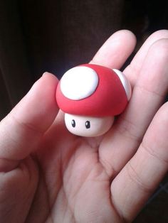 a hand holding a tiny red mushroom toy in it's left hand, with eyes drawn on the top