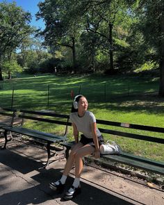 a woman is sitting on a bench in the park wearing headphones and holding her leg up