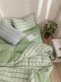 a bed with green sheets and pillows on top of it next to a potted plant