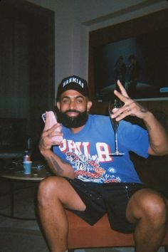 a man with a beard sitting on a chair holding a wine glass and cell phone