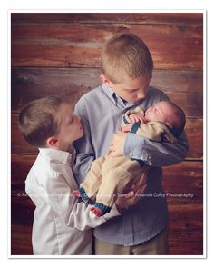 two young boys are holding their newborn babies in front of a wooden wall and looking at each other