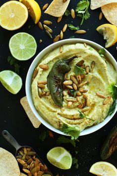 hummus in a white bowl surrounded by limes, lemon wedges and nuts