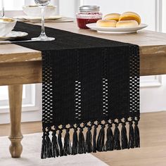 a black table runner with tassels on it and wine glasses in the background