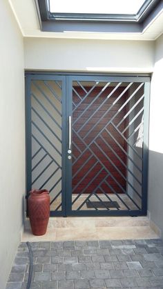 a red vase sitting in front of a glass door on a brick floor next to a white wall