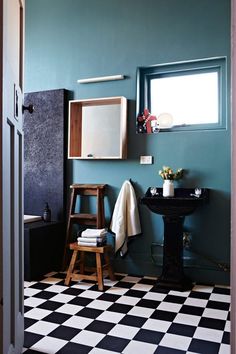 a black and white checkered floor in a bathroom with a sink, mirror and stool