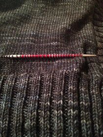 a knitted sweater with a red and white knitting needle laying on top of it