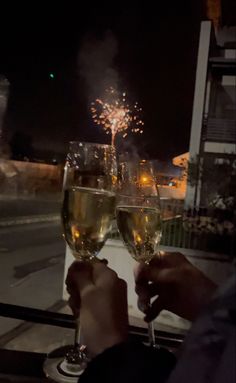 two people toasting with glasses of wine on a balcony overlooking the city at night