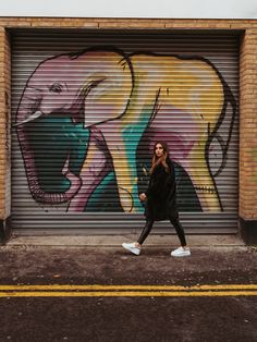 a woman walking down the street in front of a garage door with an elephant painted on it