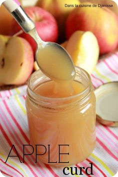 a spoon full of liquid sitting in front of some apples on a table with striped cloth