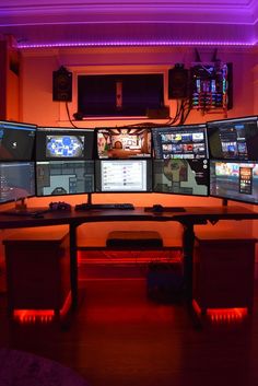 four computer monitors sitting on top of a wooden desk in front of a purple light