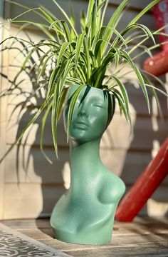 a plant in a green vase sitting on the ground next to a houseplant