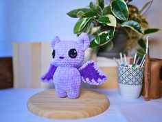 a small crocheted purple dragon sitting on top of a wooden table next to a plant