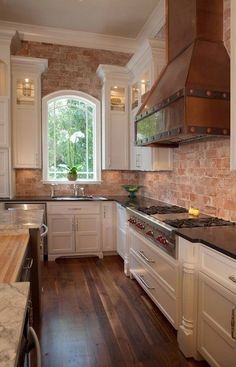 a kitchen with white cabinets and wood flooring next to a brick wall that has an arched window