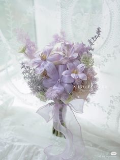 a bouquet of purple flowers sitting on top of a white cloth covered tablecloth next to a window