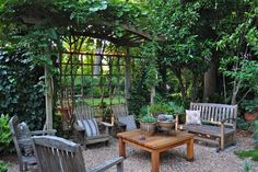 an outdoor seating area with wooden benches and chairs, surrounded by greenery in the background