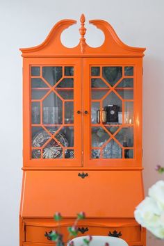 an orange china cabinet with glass doors and flowers