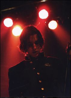 a man standing in front of red lights on stage with his hair pulled back and eyes closed