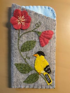 a bird sitting on top of a piece of felt next to a red and yellow flower