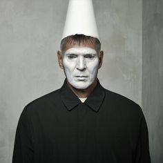 a man with white face paint on his head wearing a black shirt and a white cone hat