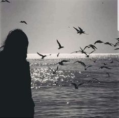 a woman standing in front of the ocean with birds flying around her