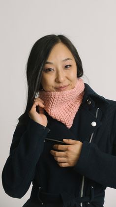 a woman wearing a black coat and pink knitted cowl scarf, posing for the camera