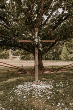 a wooden cross sitting in the middle of a grass covered field next to a tree