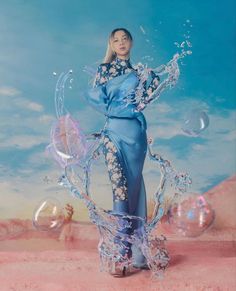 a woman in a blue dress with bubbles floating around her and the sky behind her