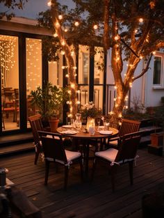 an outdoor dining area with lights strung over the table and chairs, surrounded by potted trees