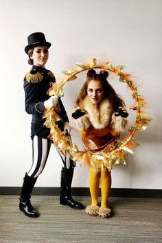 two people dressed in costumes standing next to each other with a wreath on the floor