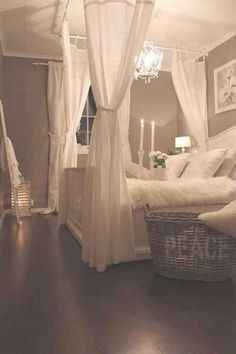 a white bed sitting in a bedroom next to a window with curtains on top of it