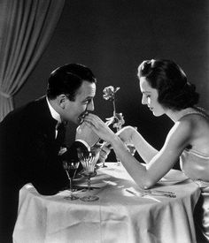 a man and woman sitting at a table with flowers in their hands