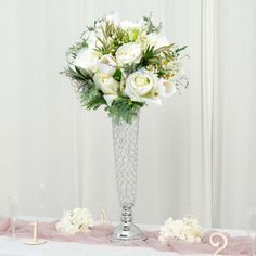 a vase filled with white flowers sitting on top of a table next to glasses and candles