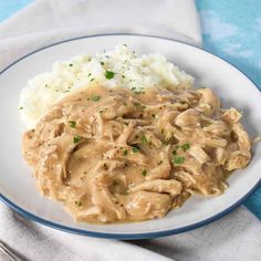 a white plate topped with meat and gravy next to mashed cauliflower