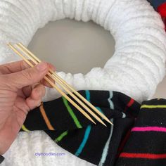 someone is holding two chopsticks in front of a wreath with yarn on it