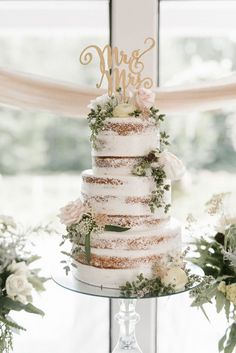 a wedding cake sitting on top of a glass table next to flowers and greenery