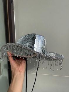 a person is holding a silver hat with chains hanging from it's brim