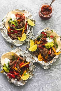 three steak fajitas on tin foil with salsa and lime wedges next to them