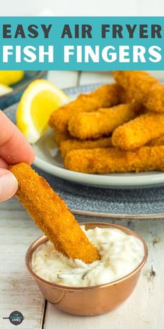 a person dipping fish fingers into a bowl of ranch dressing with lemons in the background