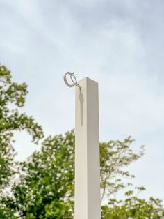 a tall white monument with a ring hanging from it's side and trees in the background