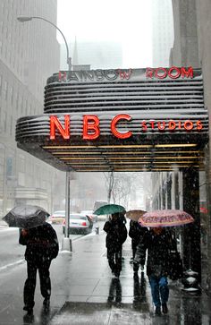 people walking under umbrellas in the rain near a theater sign that reads nbc studio