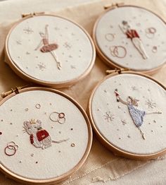 four embroidered hoop frames with little fairy characters on them, all in gold and white