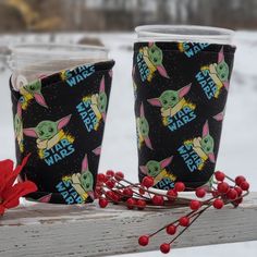 two cups sitting on top of a wooden table covered in star wars fabric and red berries