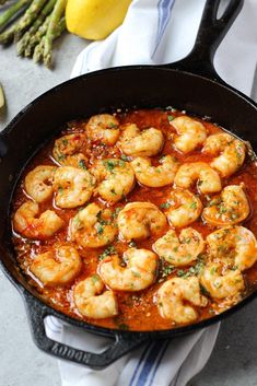 a skillet filled with shrimp and sauce next to asparagus on a towel