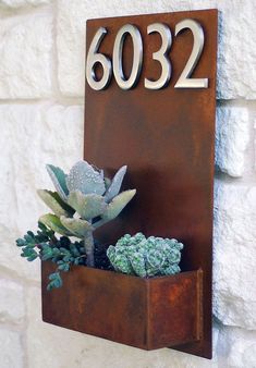 a house number sign mounted to the side of a wall with succulents in it