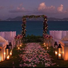 an outdoor seating area with candles and flowers on the grass next to the water at night