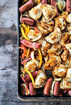 a pan filled with sausages, peppers and other vegetables on top of a wooden table