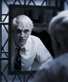 a man with white hair is looking at himself in the mirror while wearing a tie